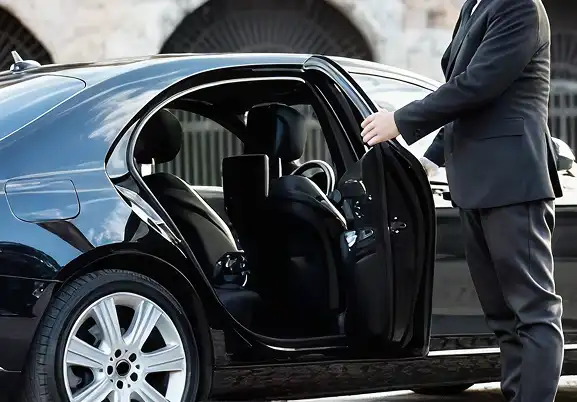 Professional chauffeur opening the door of a luxury black sedan for a passenger.