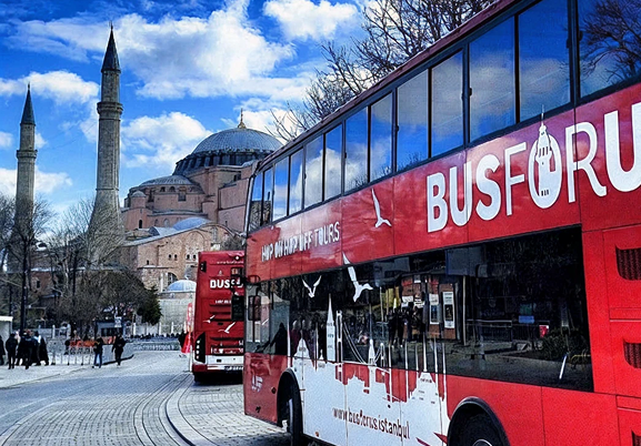 Red sightseeing bus parked in front of Hagia Sophia in Istanbul, Türkiye.